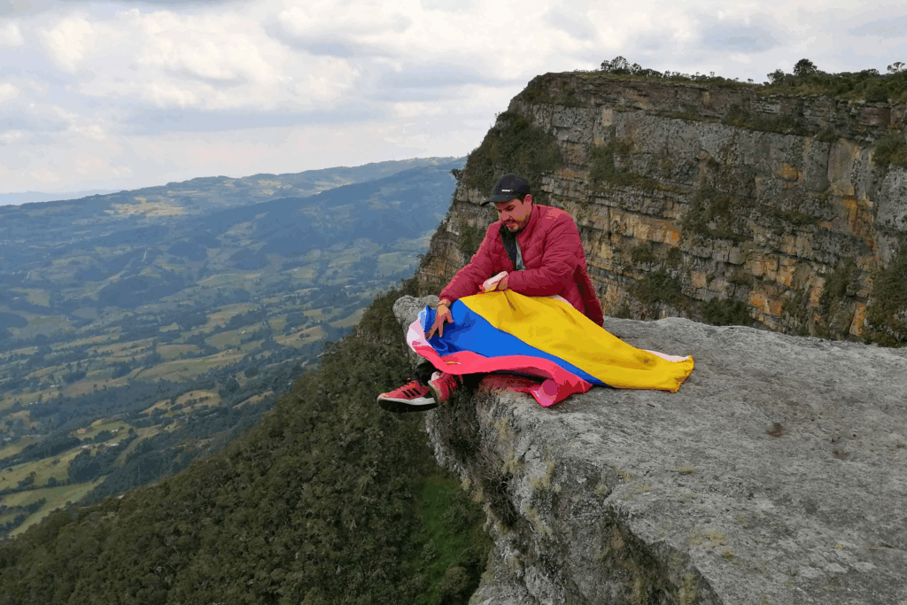 Colombiajero con la bandera de Colombia frente a la imponente Piedra Colgada, en el desierto de La Guajira. Un lugar icónico para los colombiajeros que desean descubrir los rincones más sorprendentes de Colombia.